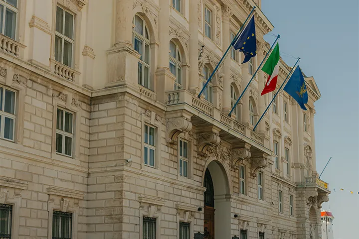 Ljus praktbyggnad med EU-flagga och italiensk flagga på fasaden